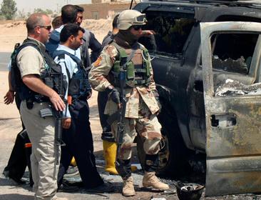 A private security contractor and soldiers look at a destroyed vehicle after an attack near Najaf, Iraq, May 18, 2006
