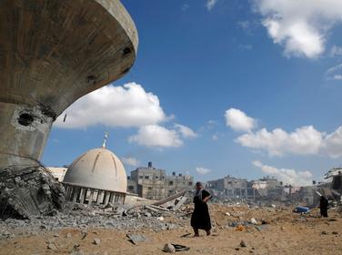 Palestinians walk past a mosque and water tower damaged by Israeli air strikes and shelling in Khuzaa, in the southern Gaza Strip