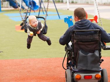 Father in wheelchair with child on swing