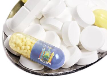 The state flag of New York on a capsule and pills on a spoon