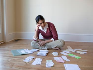 Woman seated on the floor, surrounded by bills and receipts, photo by David Sacks/Getty Images