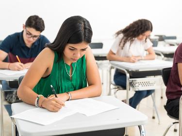 Confident student writing exam in classroom at high school, photo by AntonioDiaz/AdobeStock