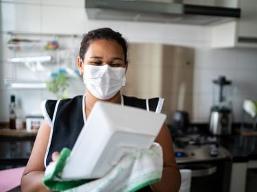 Housekeeper washing the dishes wearing a mask, photo by FG Trade/Getty Images