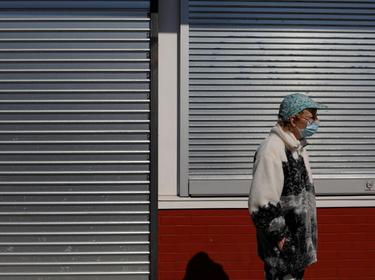 A woman waits in front of a closed and shuttered storefront amid the COVID-19 outbreak in Lynn, Massachusetts, May 4, 2020, photo by Brian Snyder/Reuters