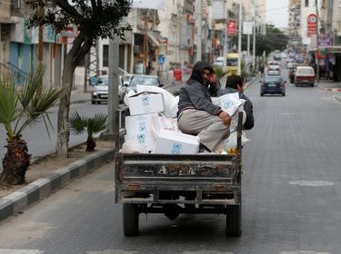 A worker rides on a vehicle transporting food supplies distributed by United Nations Relief and Works Agency to the homes of Palestinian refugees as a precaution against the spread of COVID-19, in Gaza City, March 31, 2020, photo by Mohammed Salem/Reuters