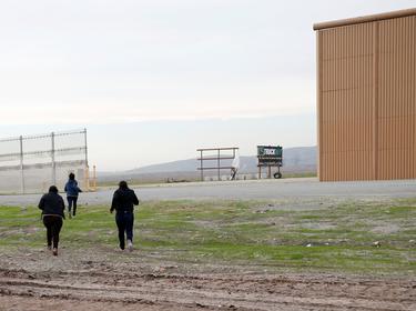 After crossing from Mexico by jumping a border fence, migrants run next to a prototype of the border wall in Otay County, California, December 21, 2018