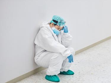Tired healthcare worker crouching in corridor, photo by Morsa Images/Getty Images