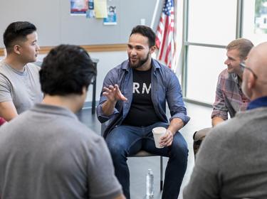 Mid adult Hispanic male veteran gestures as he discusses something during a veterans group meeting,  photo by SDI Productions/Getty Images