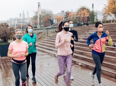 Group of women wearing face masks while running in the city during rainy and gloomy weather, photo by RgStudio/Getty Images