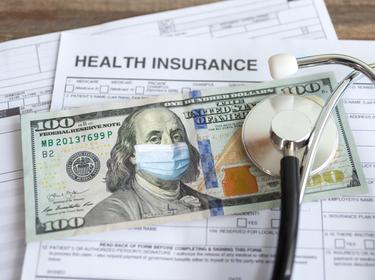Stethoscope and U.S. one hundred dollar bill with face mask on insurance form, photo by aldarinho/Getty Images
