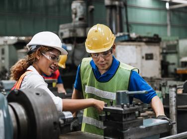 Man and woman engineer industry worker wearing hard hat in factory, photo by eakgrungenerd/AdobeStock
