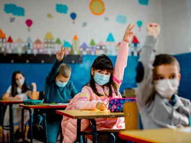 Elementary schoolchildren wearing face masks in a classroom, photo by kevajefimija/Getty Images