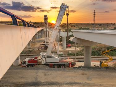 Crane trucks in the construction of a bridge, photo by Juan Enrique del Barrio/Adobe Stock