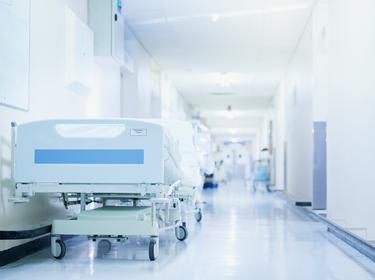 Hospital bed in a hospital corridor, photo by PeopleImages/Getty Images