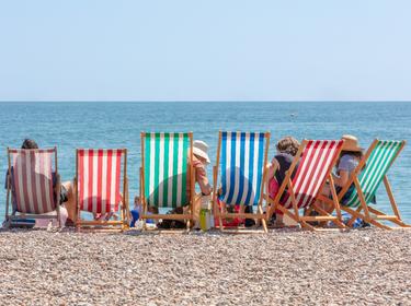 Rear view of group seated in striped deckchairs at the seaside on a sunny summer day, photo by Ian/Adobe Stock