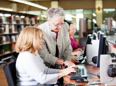 Senior librarian helping people with computers in a library, photo by Alina555/Getty Images