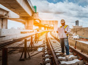 Engineer with blueprints inspects construction process on railway, photo by APchanel/Adobe Stock