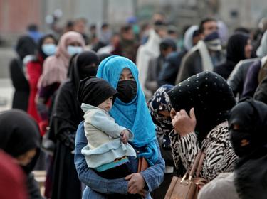 An Afghan woman holds her child as she and others wait to receive package being distributed by a Turkish humanitarian aid group in Kabul, Afghanistan, December 15, 2021, photo by Ali Khara/Reuters