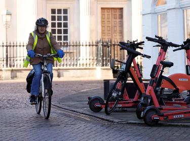 A woman cycles past parked electric scooters in Cambridge, UK, January 14, 2022, photo by Andrew Couldridge/Reuters