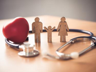 Stethoscope, heart figure, and male, female, and child figures on a table, photo by photobyphotoboy/Getty Images