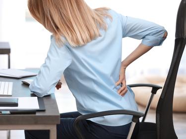 Young woman suffering from back pain in office. Photo by New Africa/AdobeStock