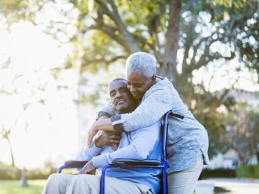 Older woman embracing older man in wheelchair, photo by kali9/Getty Images