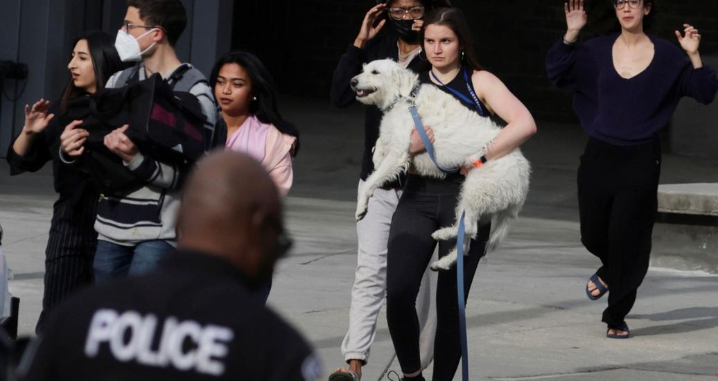 A woman evacuates with her dog in her arms as local residents are escorted by police to safety at the scene of a reported shooting near Edmund Burke Middle School in Washington, D.C., April 22, 2022, photo by Evelyn Hockstein/Reuters