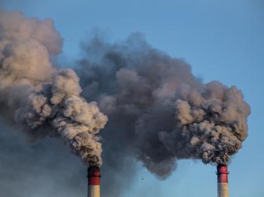 Two industrial chimneys release heavy smoke into the blue sky, photo by kapichka/Adobe Stock