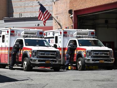 Two FDNY EMTs stand next to ambulances parked outside the Emergency entrance to Elmhurst Hospital in Queens, New York, April 28, 2022, photo by Anthony Behar/Sipa USA via Reuters Connect