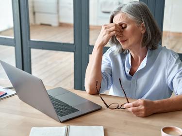 Tired woman sitting in front of a laptop, holding her head in one hand and her glasses in the other, photo by  insta_photos/Adobe Stock