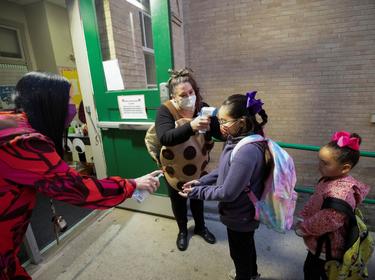 Andrew Briscoe Elementary School's principal greets and distributes hand sanitizer to students while a teacher takes their temperature before they enter the building, in San Antonio, Texas, January 11, 2022, photo by Kaylee Greenlee Beal/Reuters